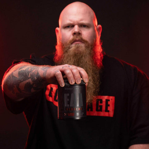 Muscular bearded man holding a container of Berserk EAAs 500g supplement for muscle growth and hydration