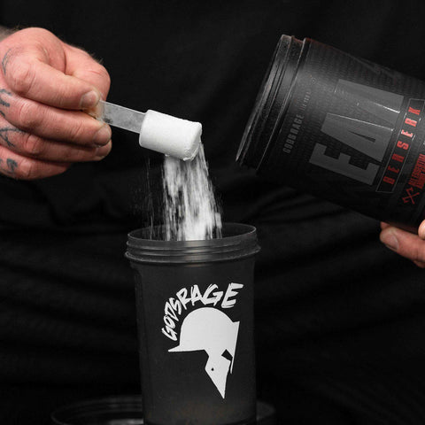 Berserk EAAs 500g powder being scooped into a black Gotsrage shaker for muscle building and hydration.