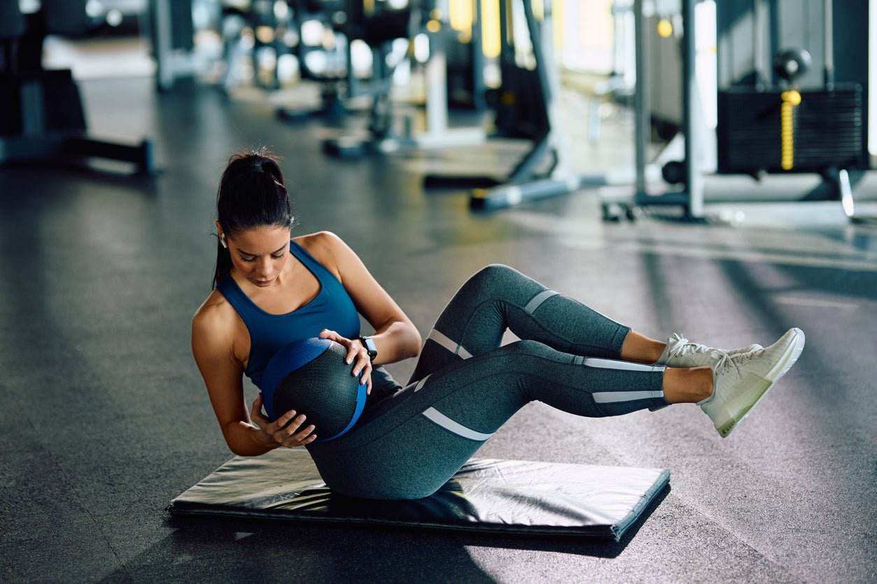 Woman doing core exercise with medicine ball on gym mat demonstrating fatburner workout effects