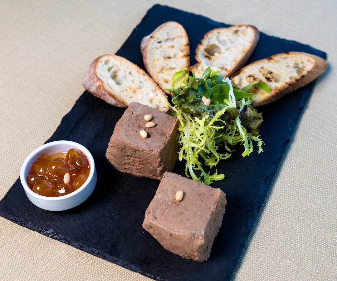 Slate serving board with pâté cubes, mixed greens, toasted bread slices, and a small dish of chutney, illustrating balanced portion sizes for athletes.