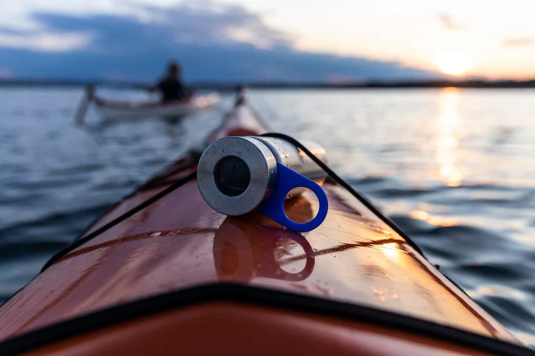 Close-up of a water bottle cap on a kayak paddle with a person kayaking on calm water during sunset, illustrating the importance of hydration and the role of water in the body for athletes.