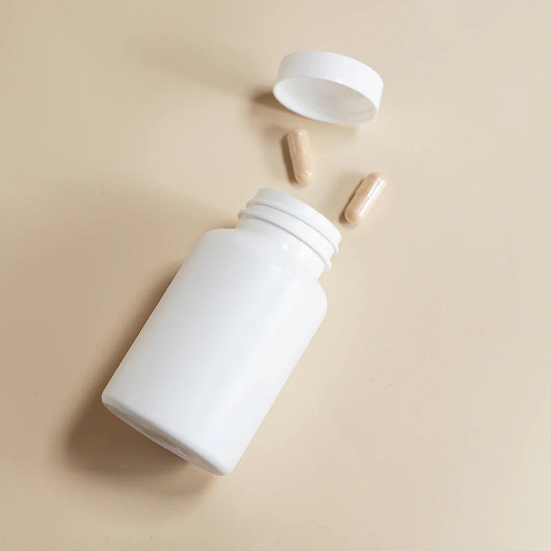 White supplement bottle with two beige capsules and an open lid on beige background representing supplements for athletes