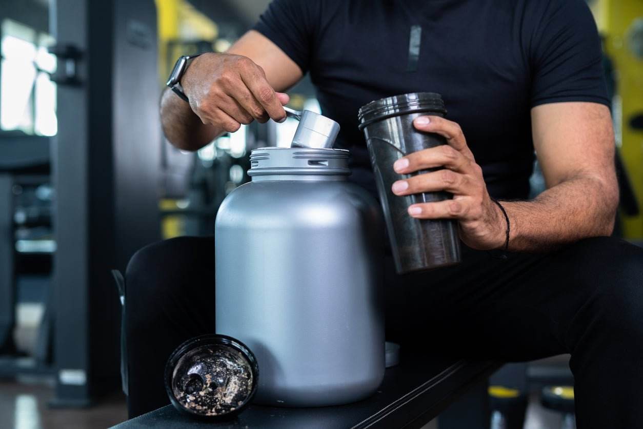 Man scooping protein powder into shaker bottle at gym for muscle building and nutrition guidance