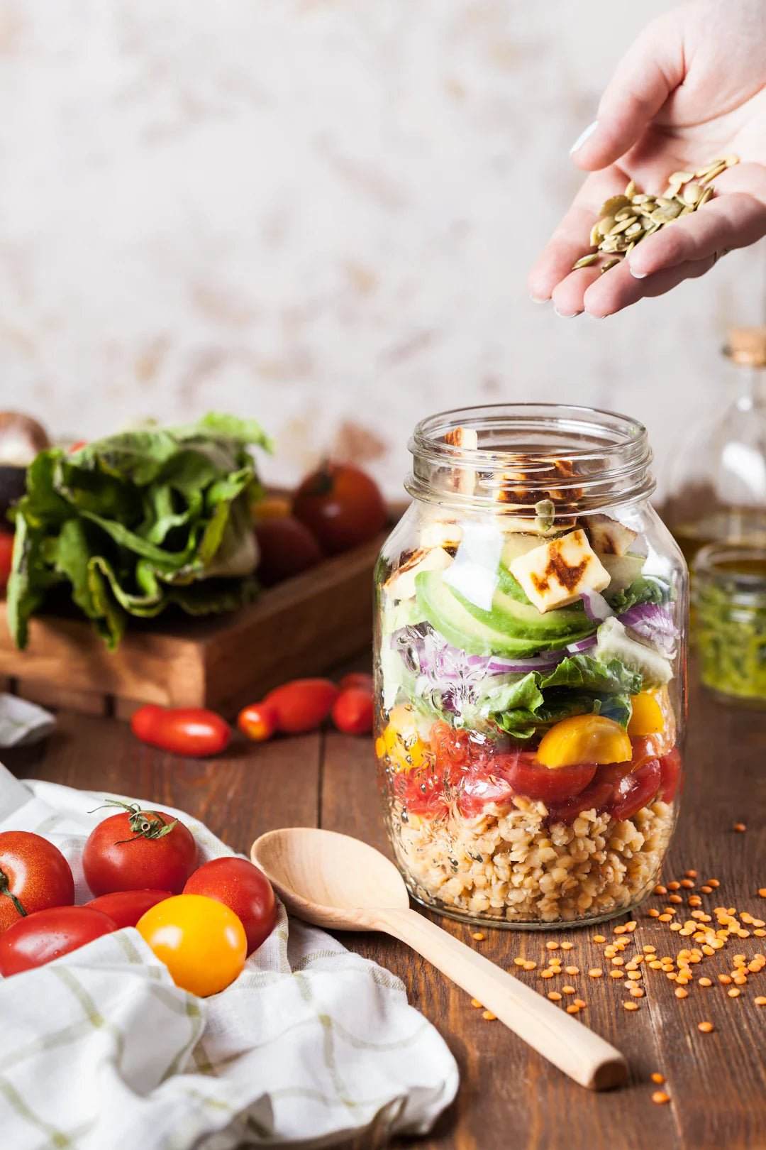 Hand adding seeds to a jar layered with fresh vegetables and grains, symbolizing vitamins and minerals for athletes' nutrition.